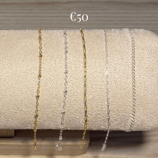 selection of thin style gold-filled and sterling silver chain for permanent jewellery laid over a cream display