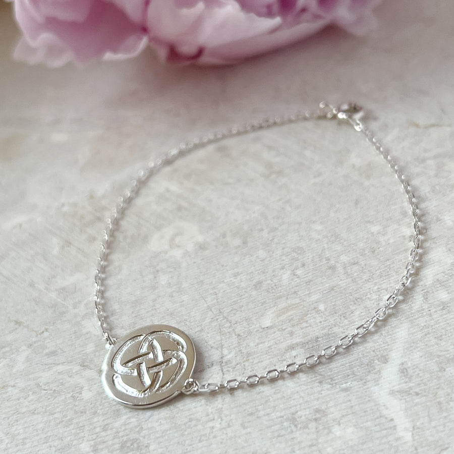 Dara Knot sterling silver strength bracelet resting against stone with a pink flower petal in the background