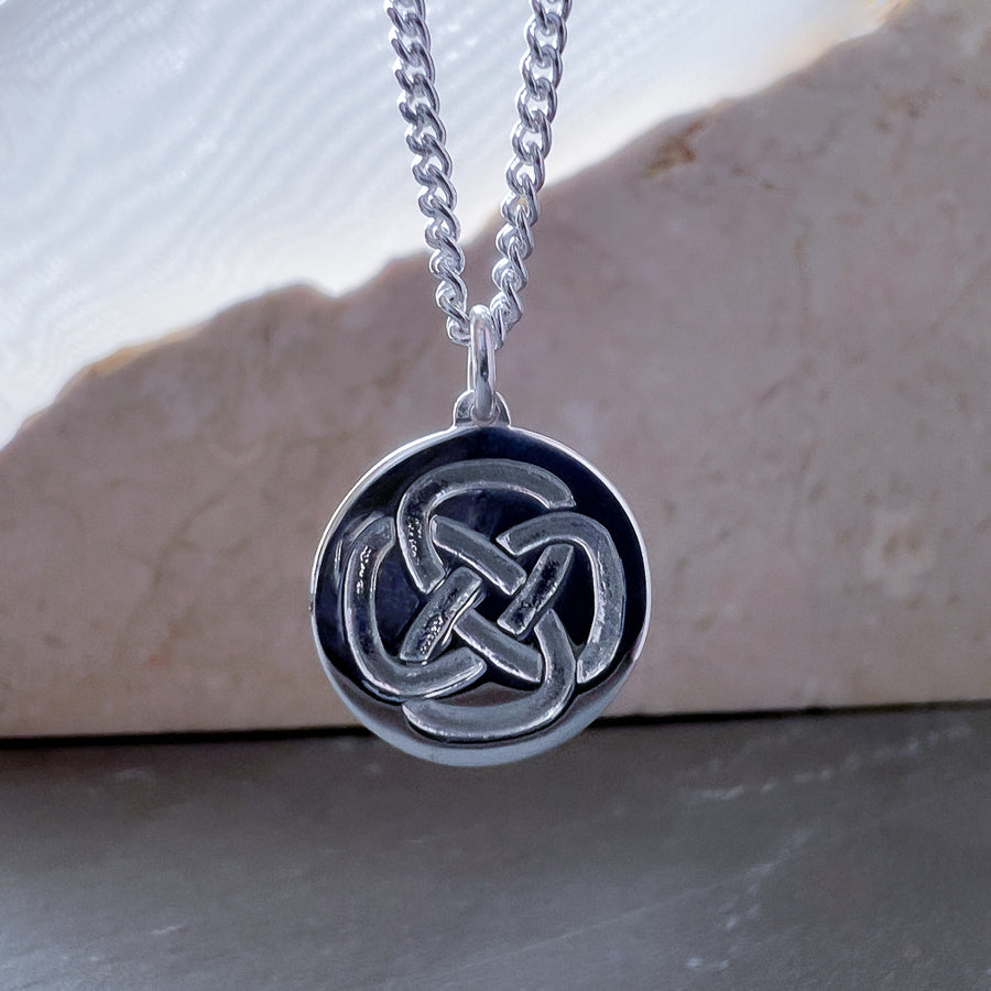 A men's sterling silver necklace symbolic for strength hanging in front of stone 